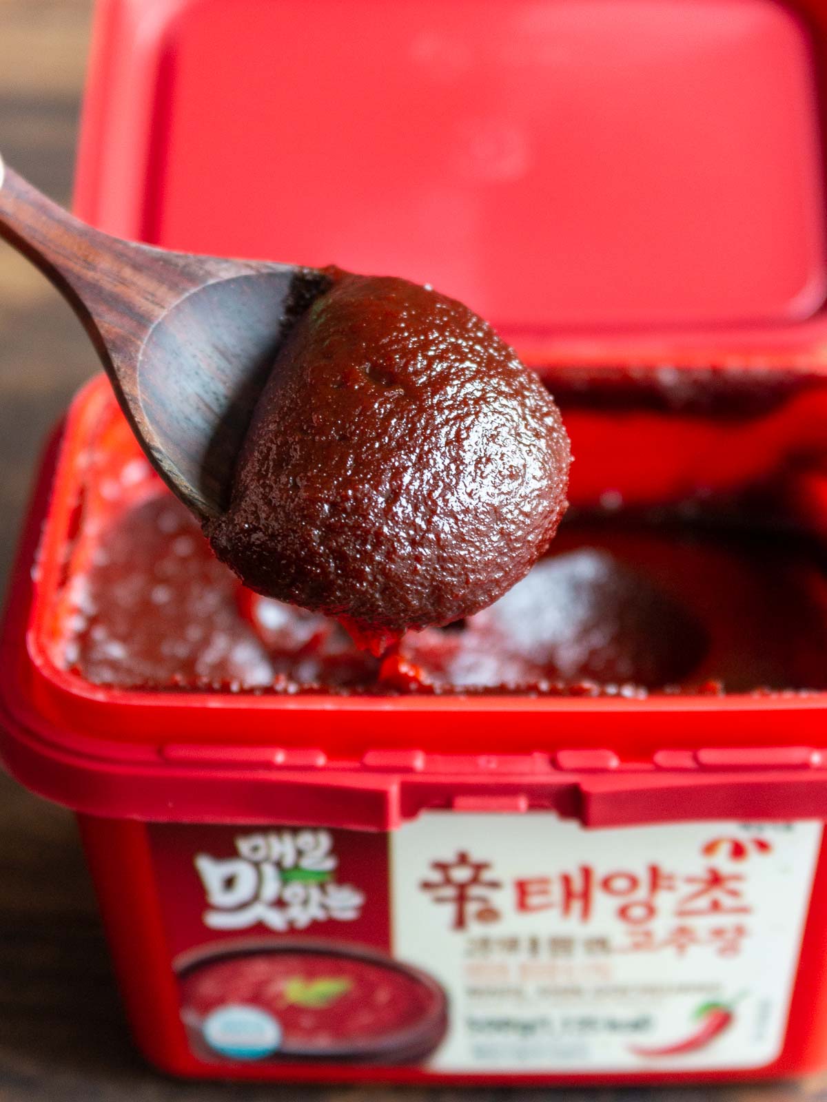 An opened container of gochujang paste with a spoonful taken out.