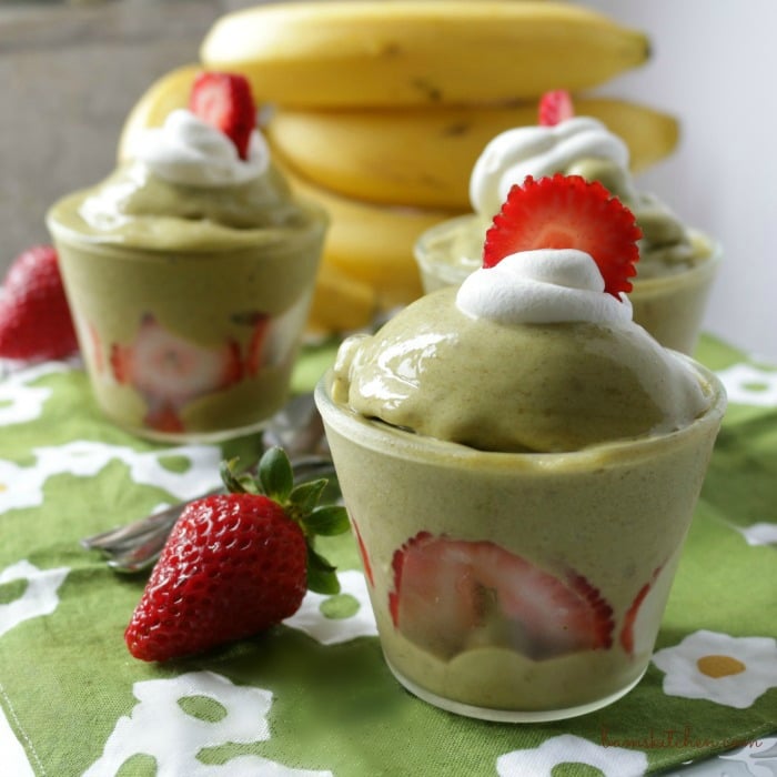 2 cups of matcha nice cream with a dollop of coconut whipped topping and a few bananas in the background.