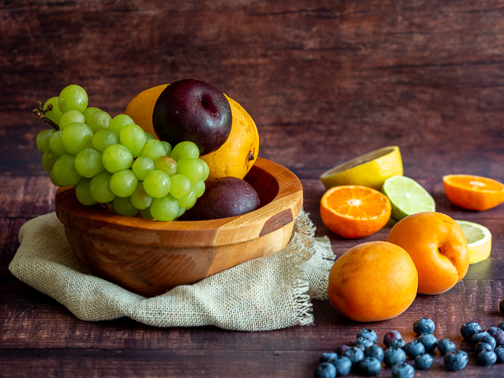 Fruit basket overflowing with mangoes, grapes, citrus and nectarines.