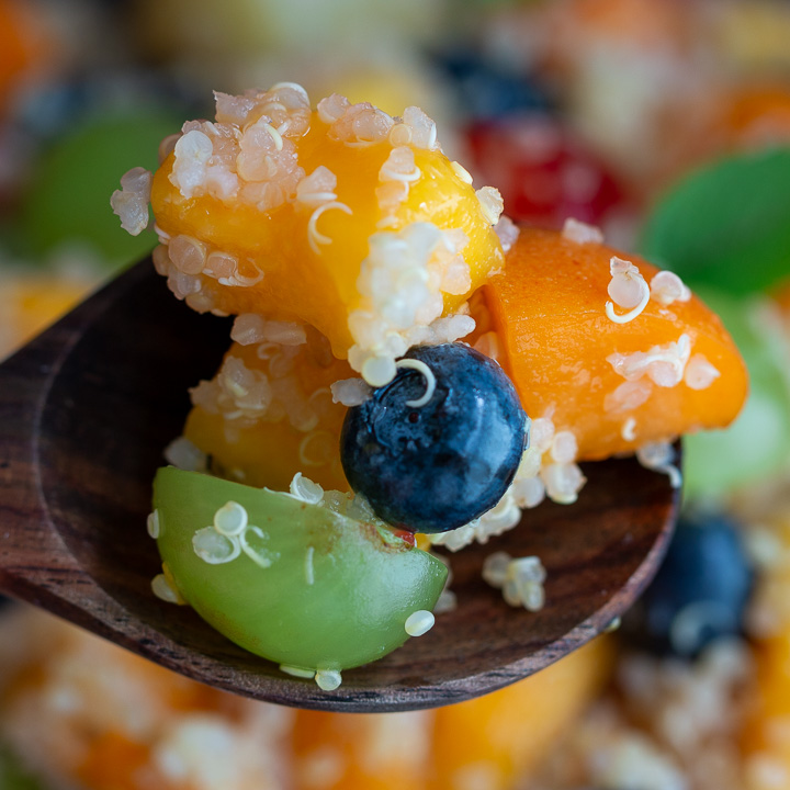 The bite shot with quinoa, mango, grapes and blueberries on a wooden spoon.