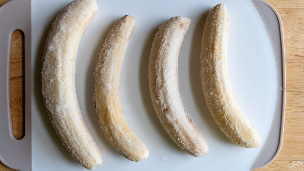 Frozen bananas laid out on a white cutting board. 