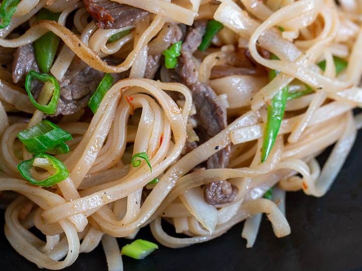 Close up shot of pan fried noodles perfectly cook and on a black dish.