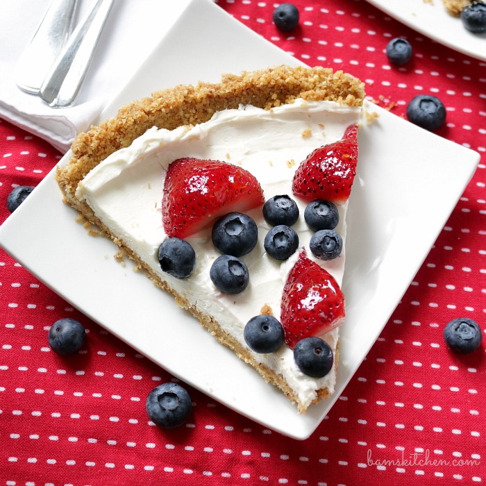 Slice of berry cheesecake on a white plate with a red and white napkin. Garnished with blueberries and strawberries.