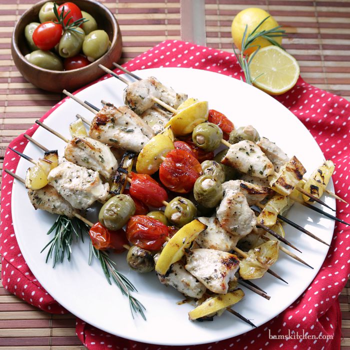 Mediterranean Chicken Kabobs on a white plate garnished with rosemary and lemons.