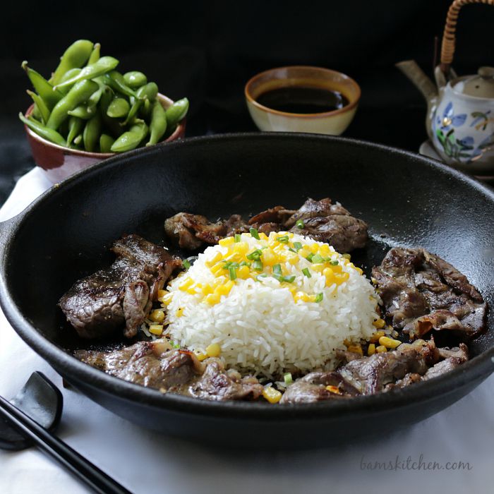 Bowl of pepper beef with a mound of rice with corn and green onions on top. 