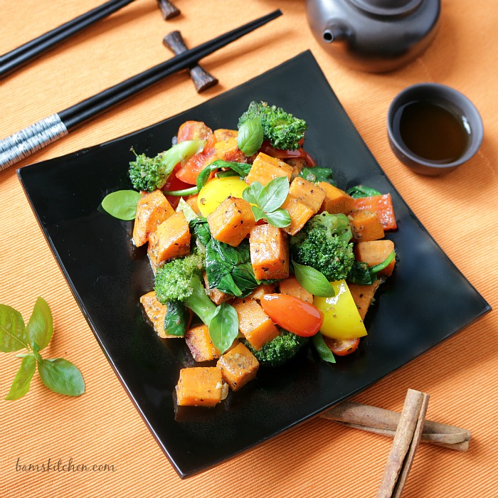 Vegetable stir fry on a black plate with chop sticks and Chinese Tea.