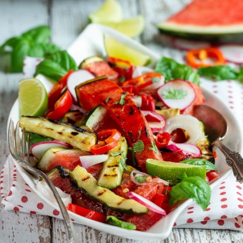 Plate of deliciously grilled watermelon and cucumbers tossed in a Thai dressing on a white plate with a red and white polka dot napkin.