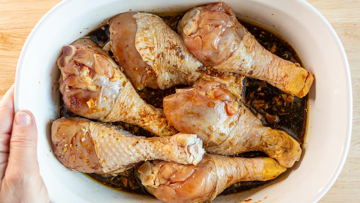 chicken legs marinating in a white bowl.