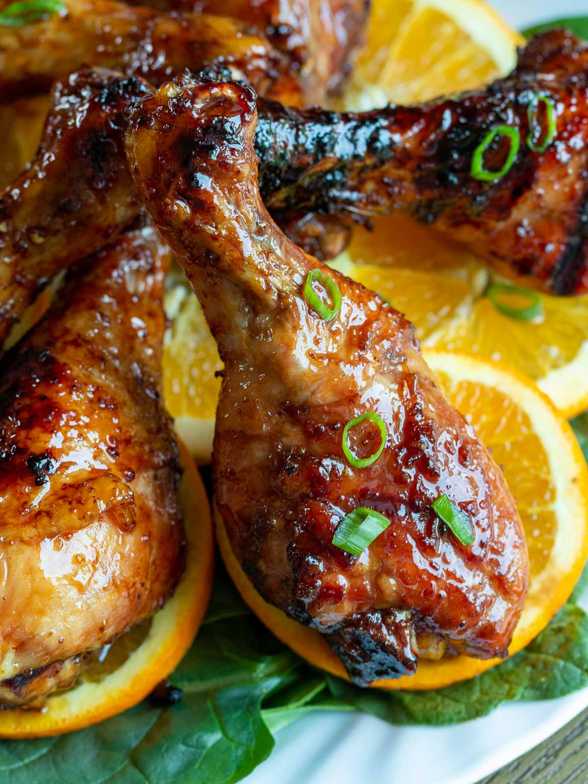 Grilled chicken legs stacked on an angle on a plate lined with oranges and greens.