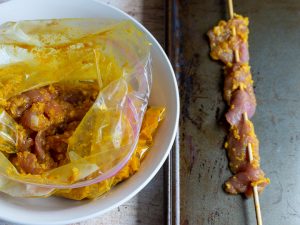 Marinated pork getting placed on wooden skewers.