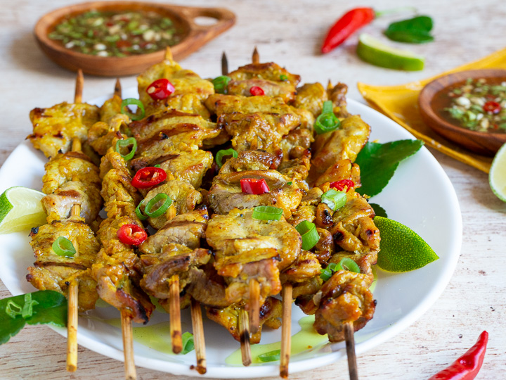 Perfectly tender grill pork tenderloins on skewers with prik nam pla sauce in wooden bowls. 