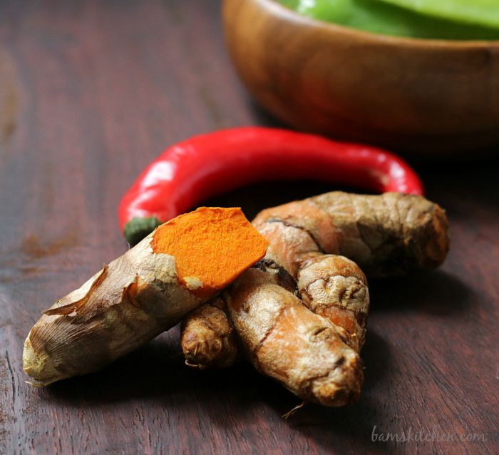 Fresh turmeric root and a chili pepper on a wooden cutting board. 