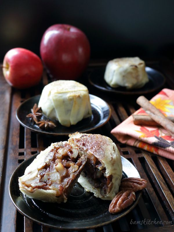 3 apple pecan mooncakes on black plates with apples and spice scattered around the plates.