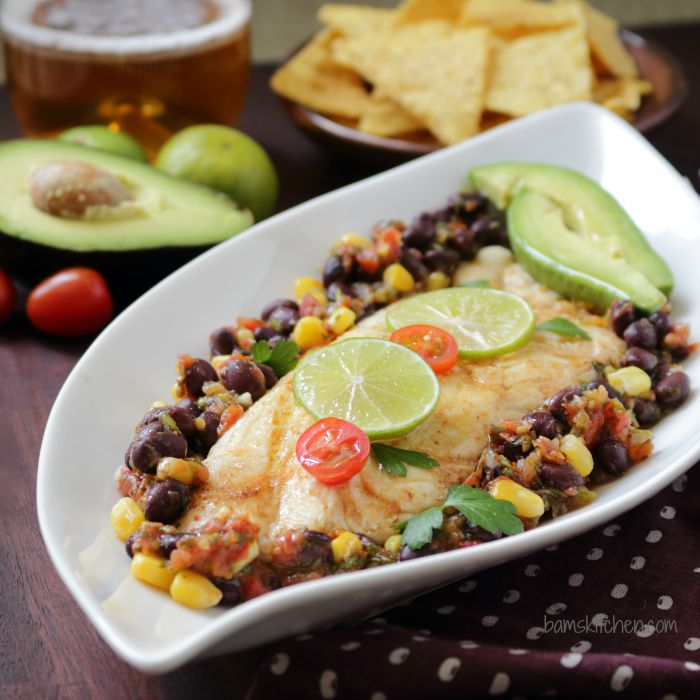 Baked Skinny TEX MEX Fish in a white dish garnished with limes and tomatoes.