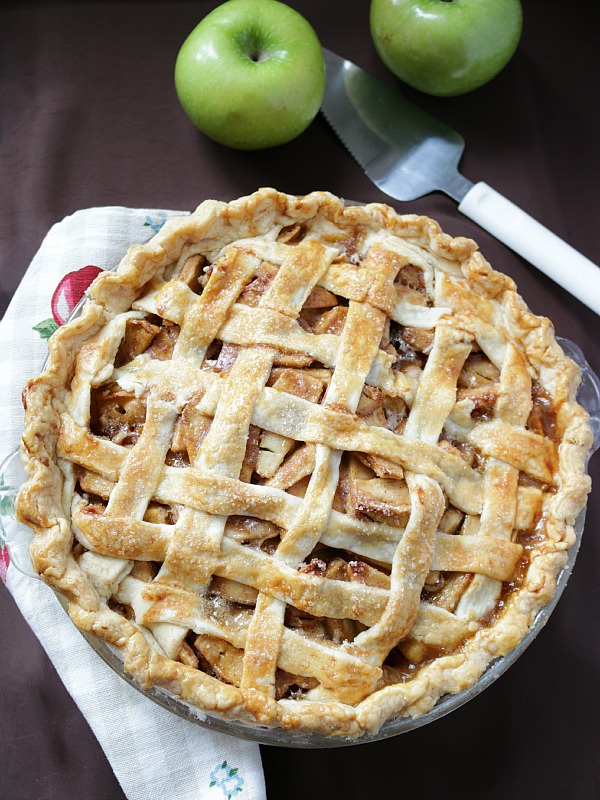 Top down shot of a grandma's apple pie hot out of the oven with apples and a knife on the table.
