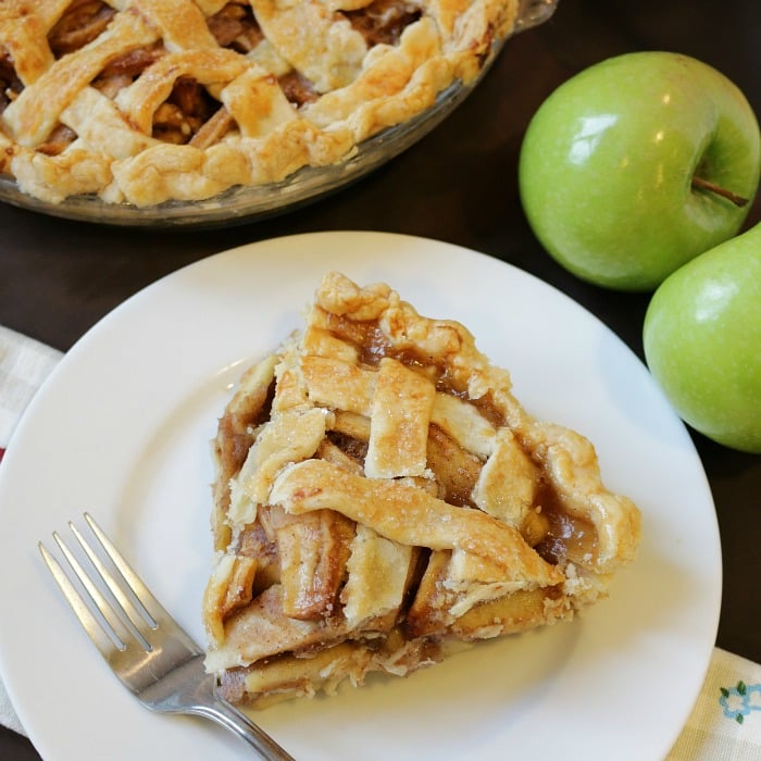 Slice of apple cinnamon pie on a white plate with a fork.