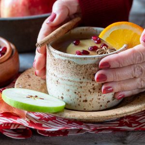 Hands wrapped around a cozy mug of hot apple cider.