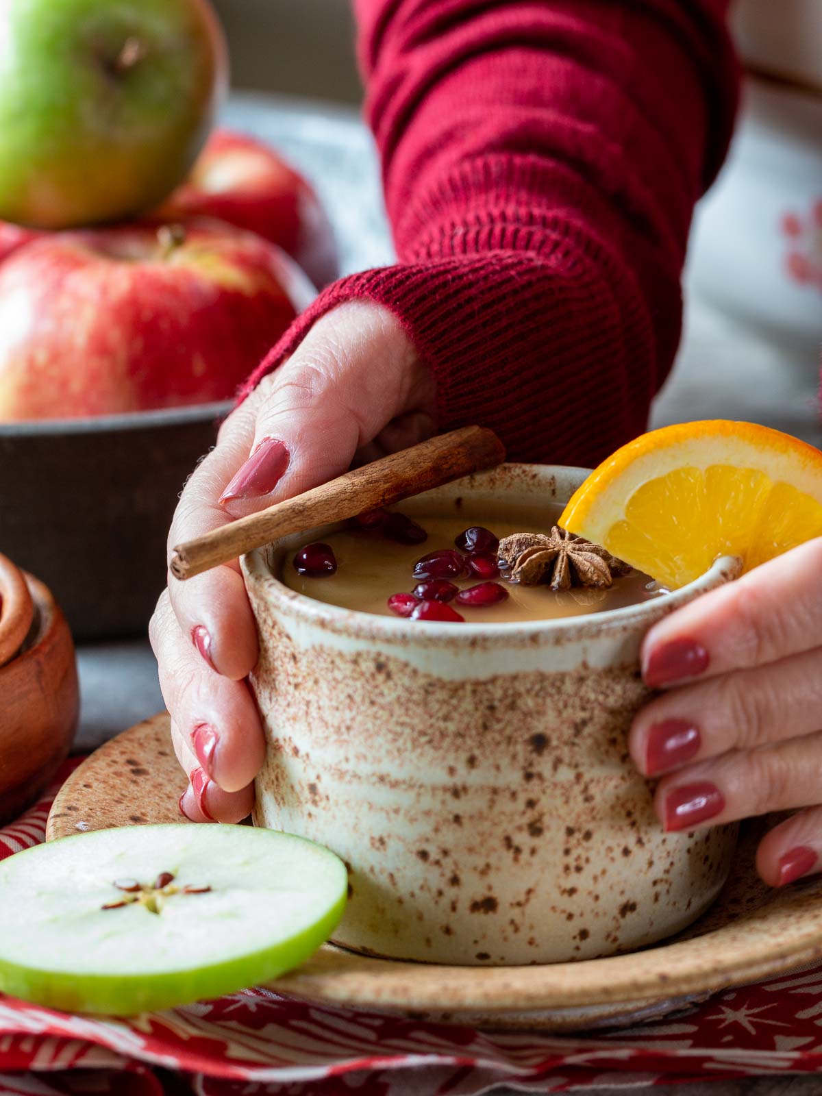 Holding a cup of spicy hot cider in hands with a cozy red sweater on.