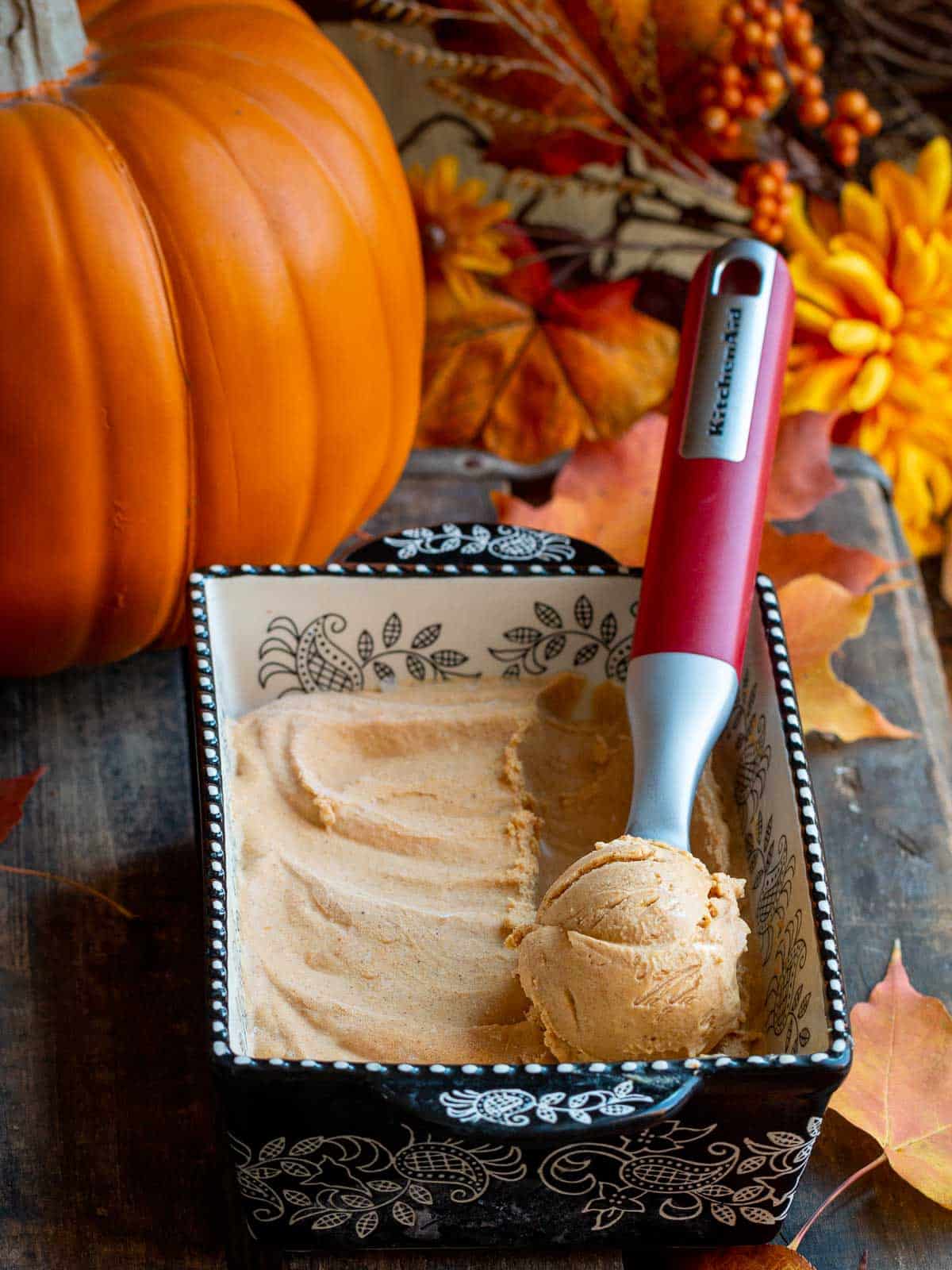 Dairy free pumpkin ice cream in a black and white pan with a red ice cream scoop with a scoop in it.