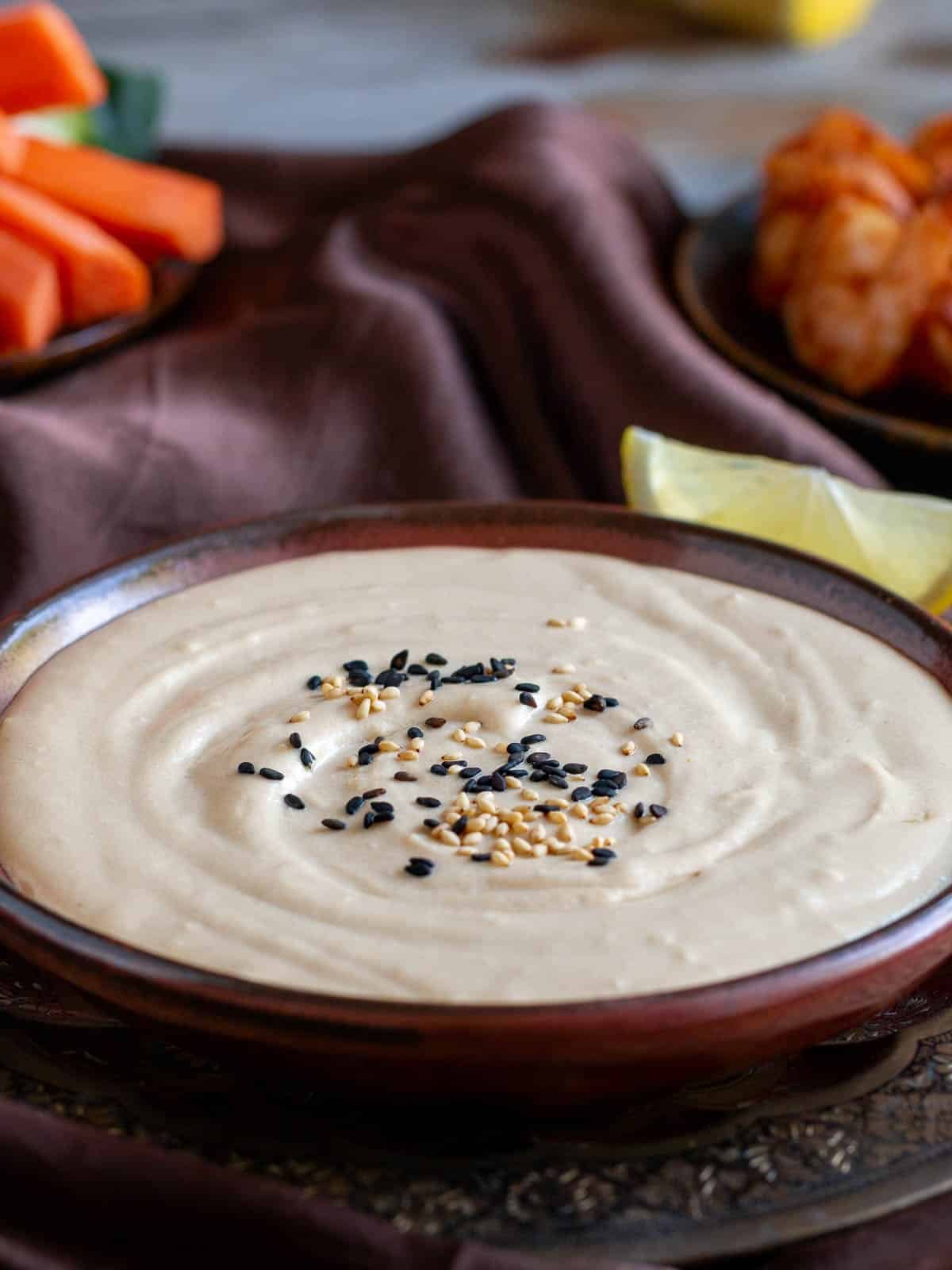 Ready to eat Middle Eastern dip in a handmade brown pottery bowl garnished with sesame seeds.
