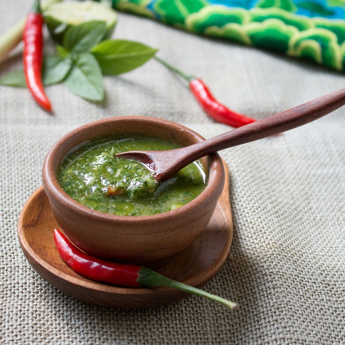 Thai Style Chimichurri sauce in a wooden bowl surrounded by red chili peppers.