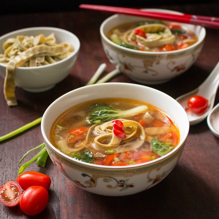 2 bowl of tomato mung bean noodle soup this red chopsticks and fresh tomatoes arranged around the bowls.