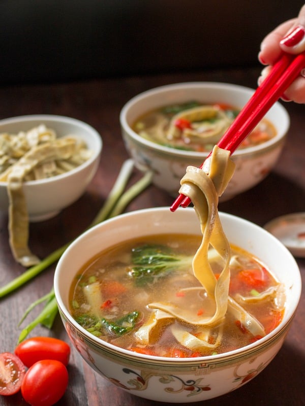Mung Bean noodles tossed around red chopsticks from a bowl of delicious soup. 