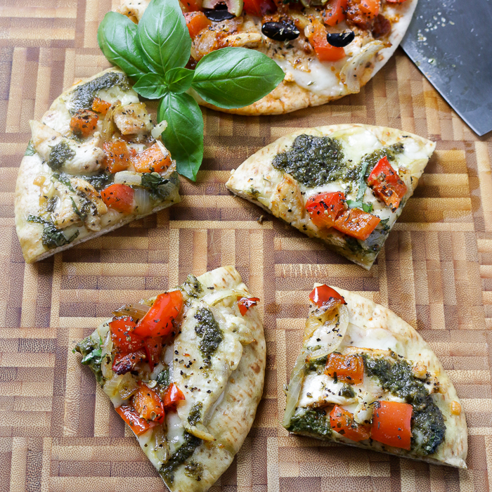 Pita pizzas on a cutting board cut into fouths.