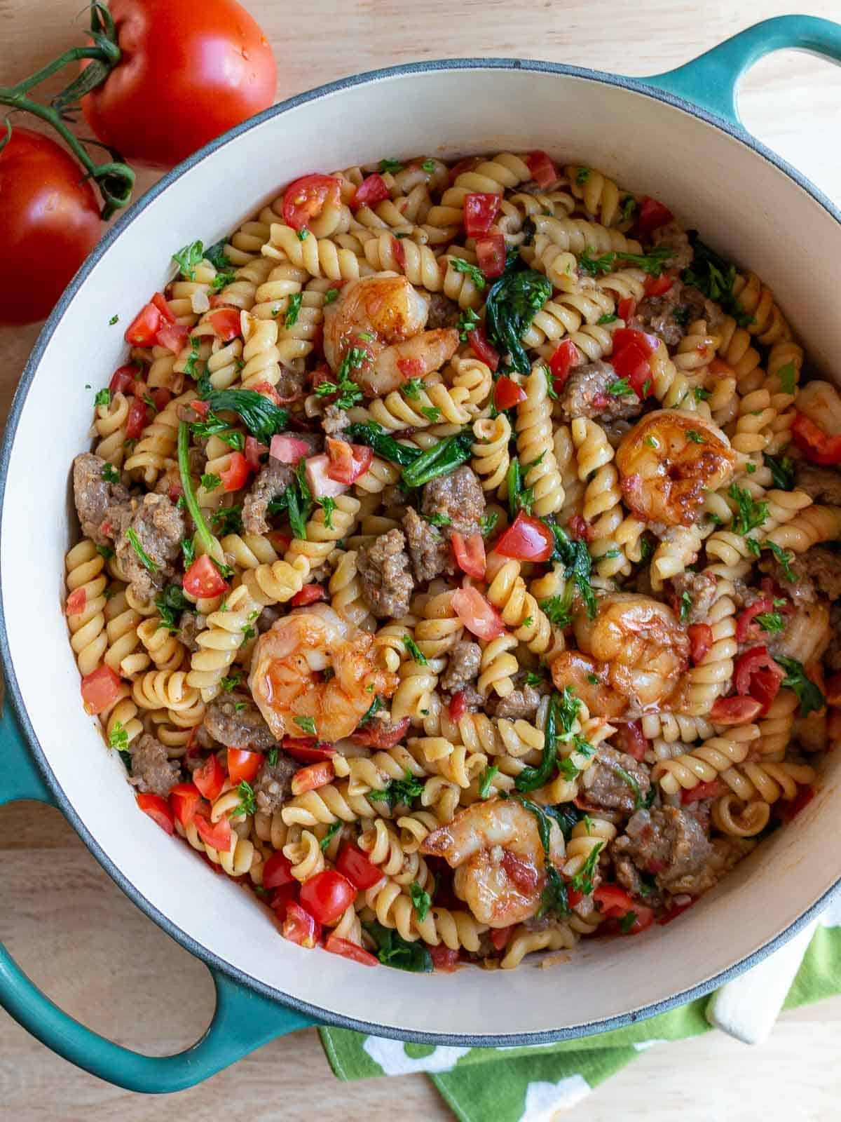 Shrimp and Italian sausage pasta served in a green pot.