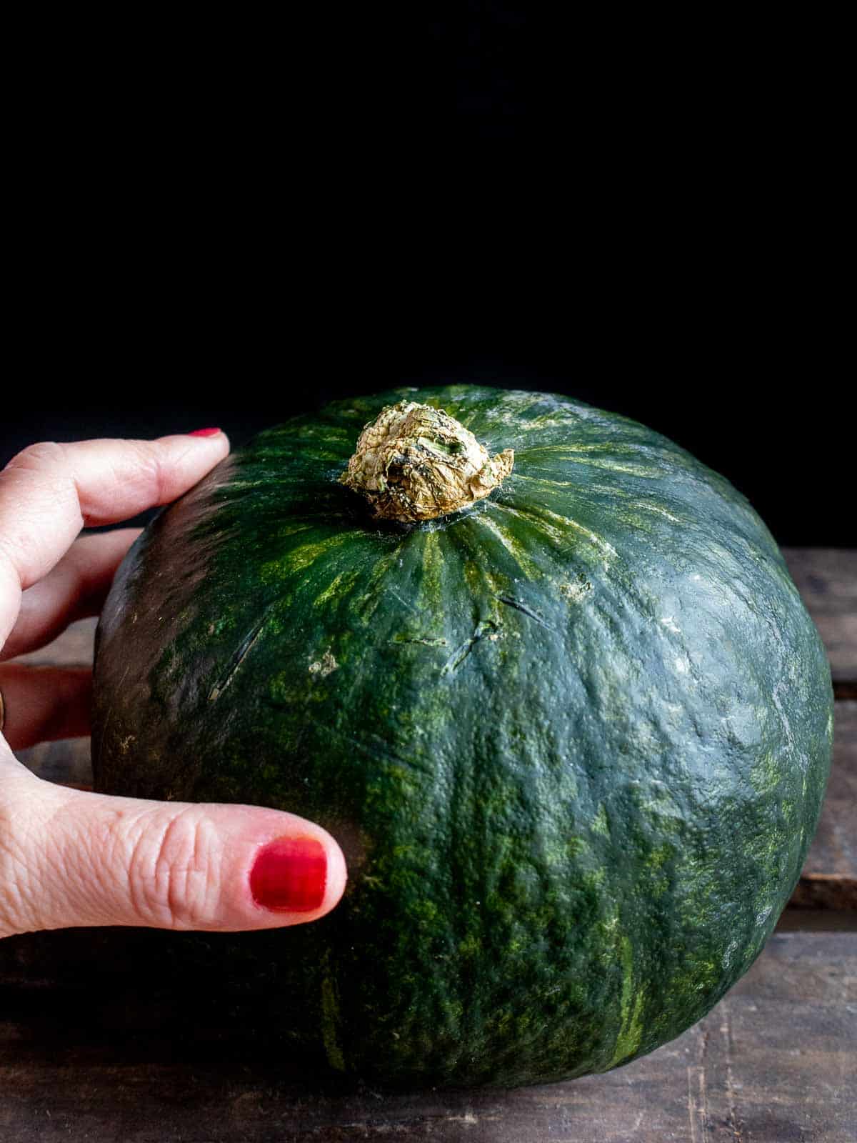Whole kabocha squash being held by a hand.