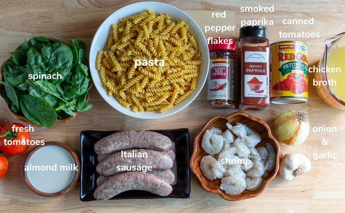 Ingredients such as pasta and sausage and seasonings are laid out on a cutting board.