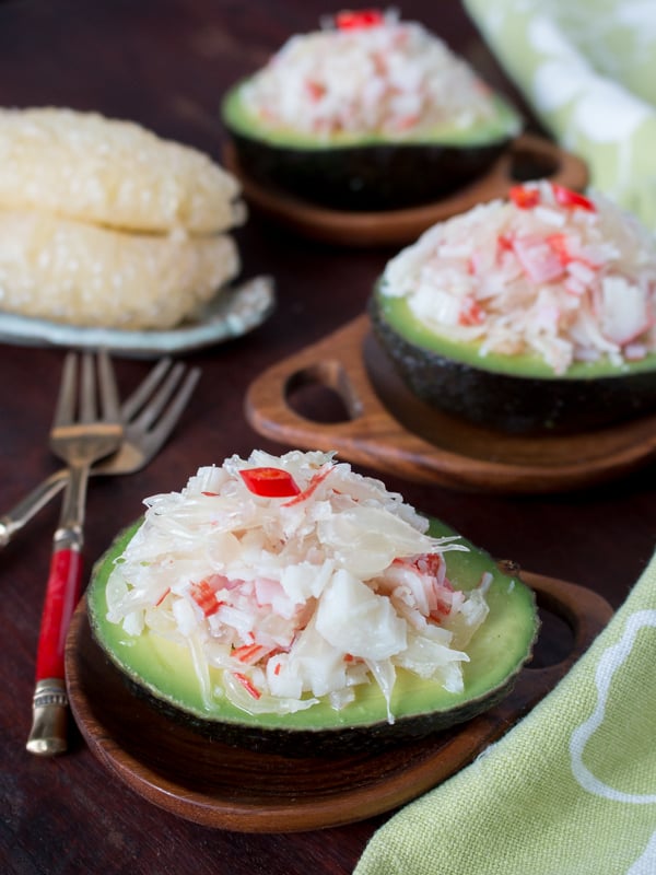 3 Avocado boats filled with the crab and pomelo dressing with while sections of pomelo in a dish and forks. 