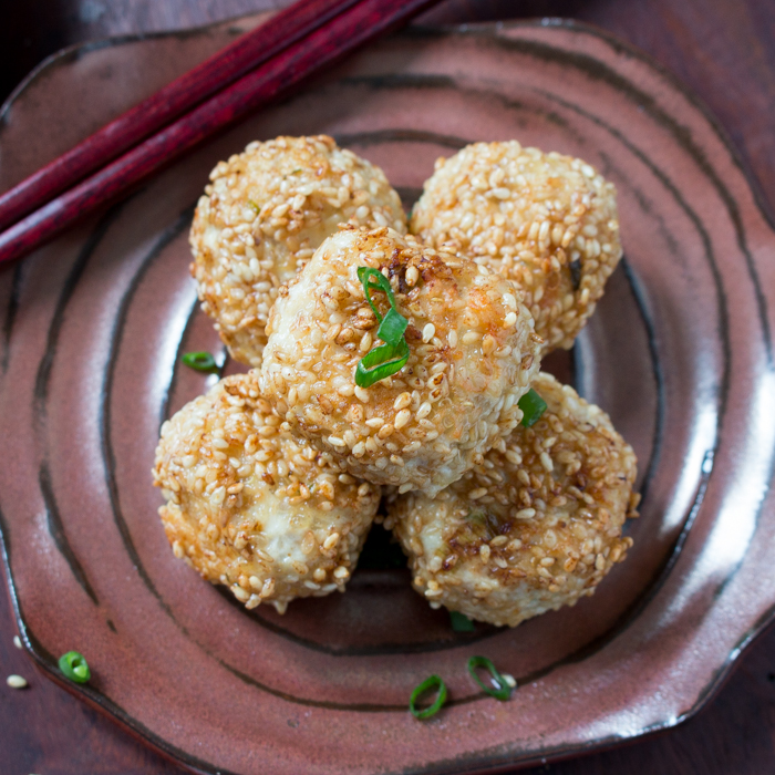 Five sesame chicken meatballs stacked on a brown homemade Japanese pottery plate with chopsticks.