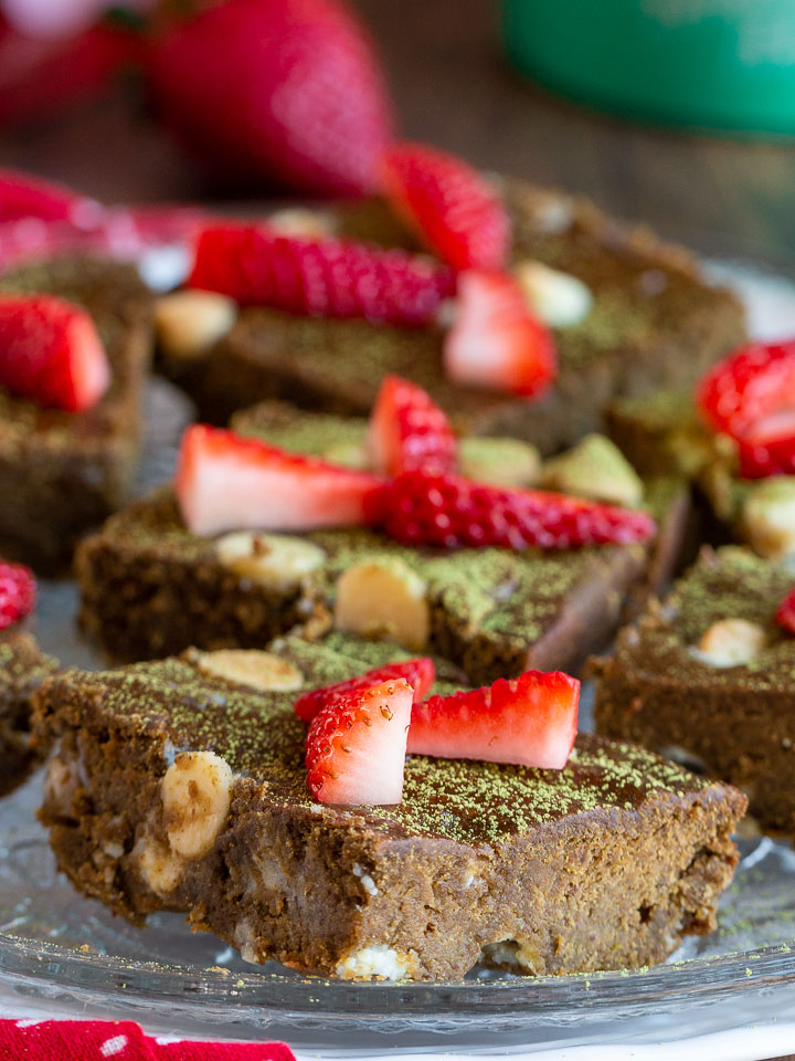 Many matcha brownies laid out on a white plate topped with strawberries.