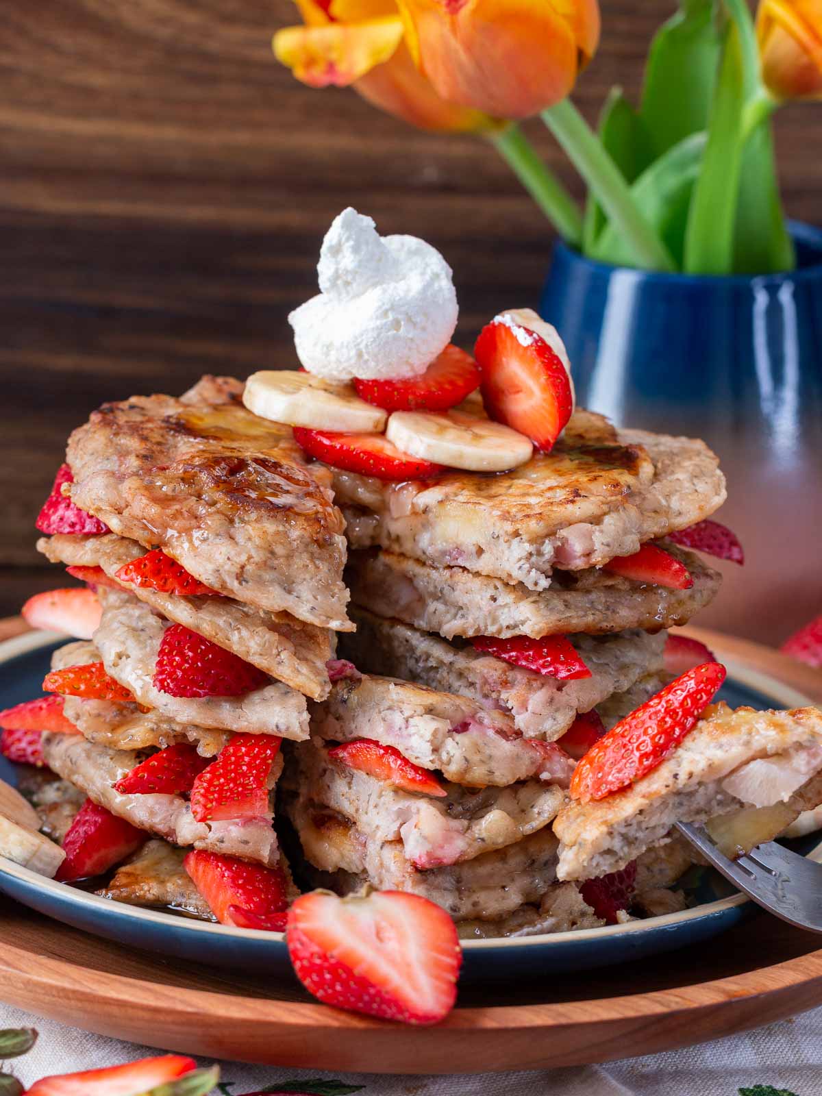 The bite shot with pancake and strawberries on a fork with a plate of flapjacks.