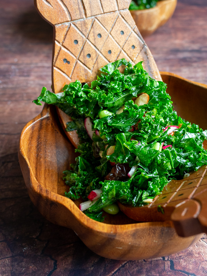 Salad getting placed into wooden bowls.