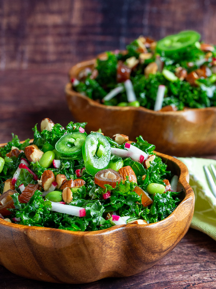 Two huge bowls of salad in wooden vessels with a fork and green napkin.