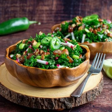 Two wooden bowls filled with autumn kale salad on a wooden board.