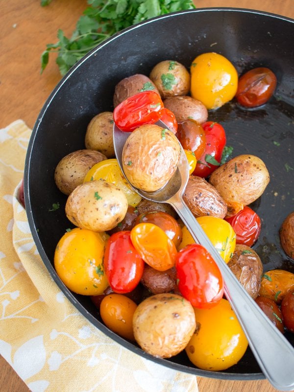 Potatoes and tomatoes in an iron skillet getting tossed in the brown butter.