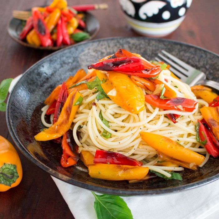 Mini roasted peppers piled high on top a bed of pasta with lots of fresh basil in a black plate.