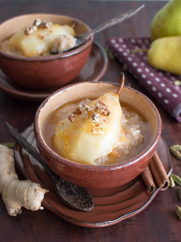 2 bowls of rice pudding with a half pear with the stem and sprinkled with pecans.