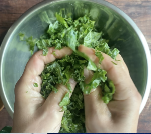 Kale getting massaged between fingers with olive oil and salt.