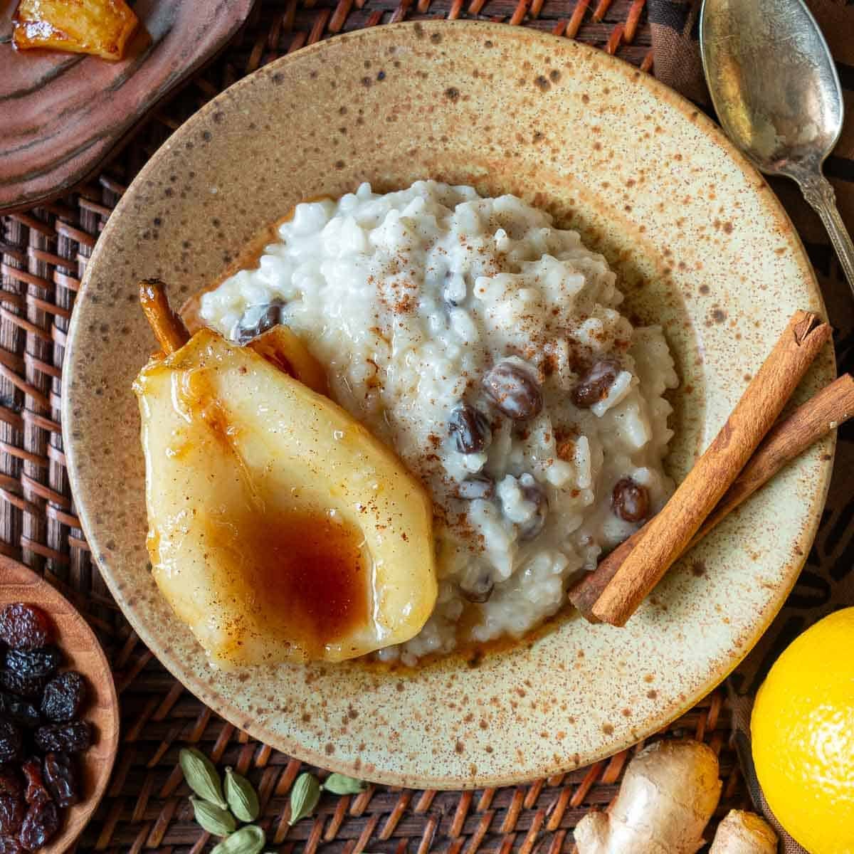 Coconut rice pudding made with coconut milk, almond milk and sweetened condensed milk on a beige plate topped with cinnamon twills and poached pears. 