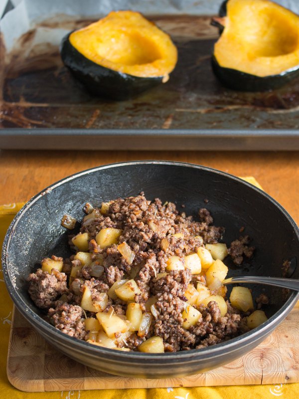 Double meat and apple mixture in an iron skillet with halves of cooked acorn squash in the background.