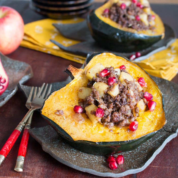 Baked acorn squash stuffed with 2 kinds of meat and apples and garnished with pomegranate  seeds on handmade japanese pottery dishes shaped like a leaf. 