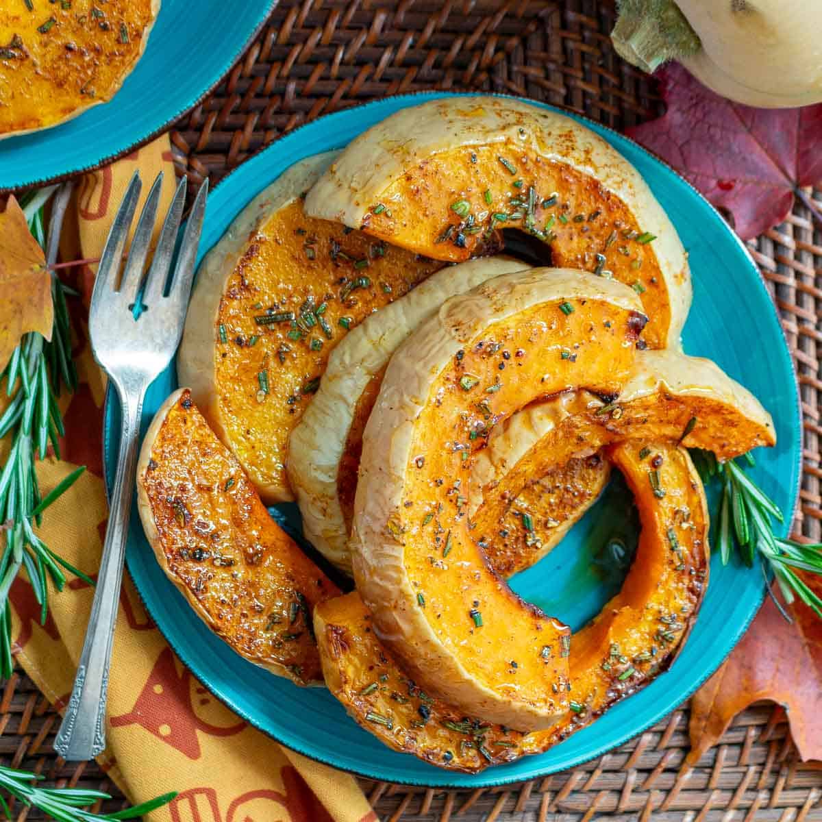 Cozy fall shot of roasted squash on a blue plate with leaves and rosemary. 