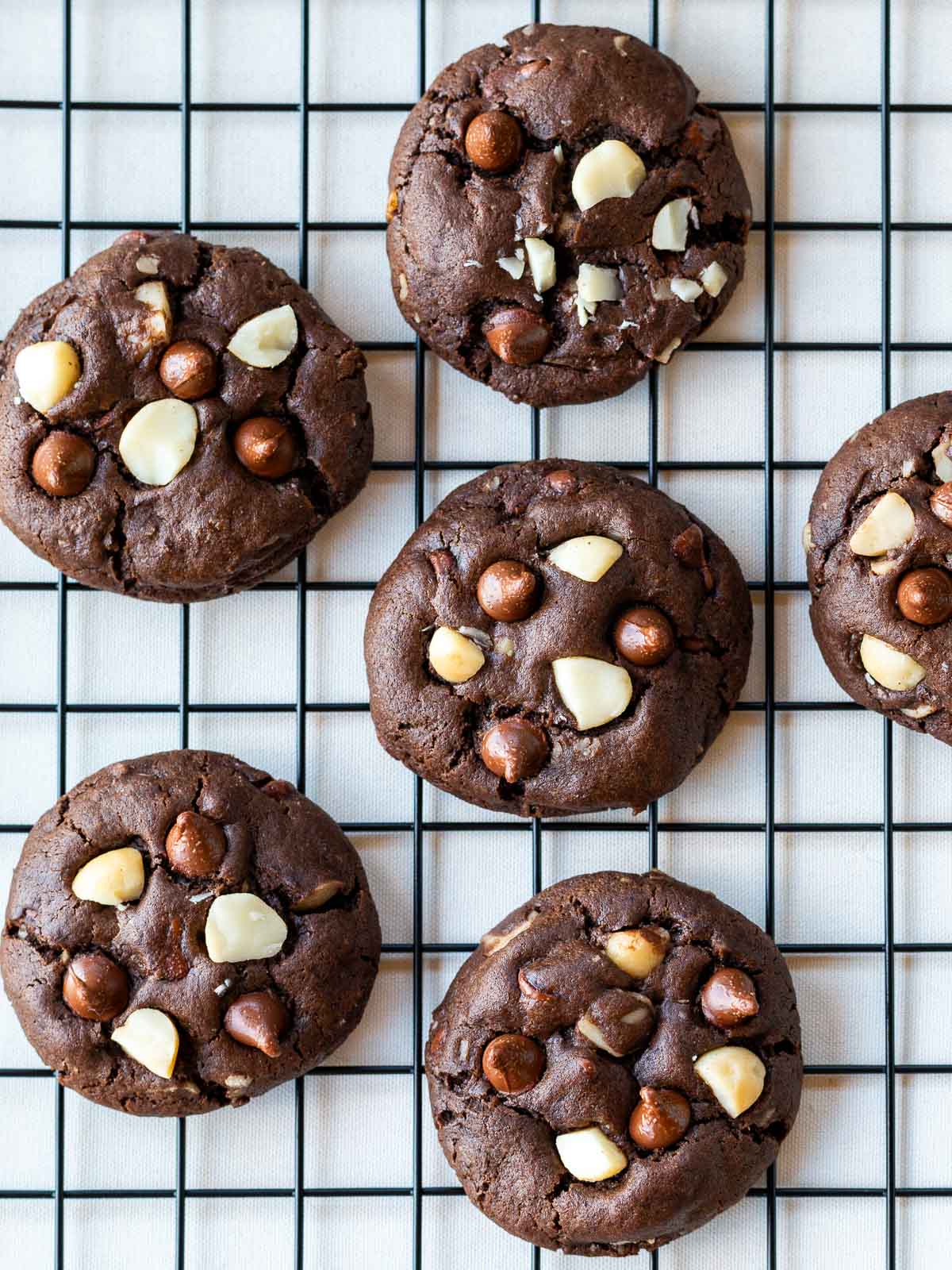 Freshy baked chewy chocolate cookies studded with macadamia nuts and chocolate chips cooling on a cooling rack. 
