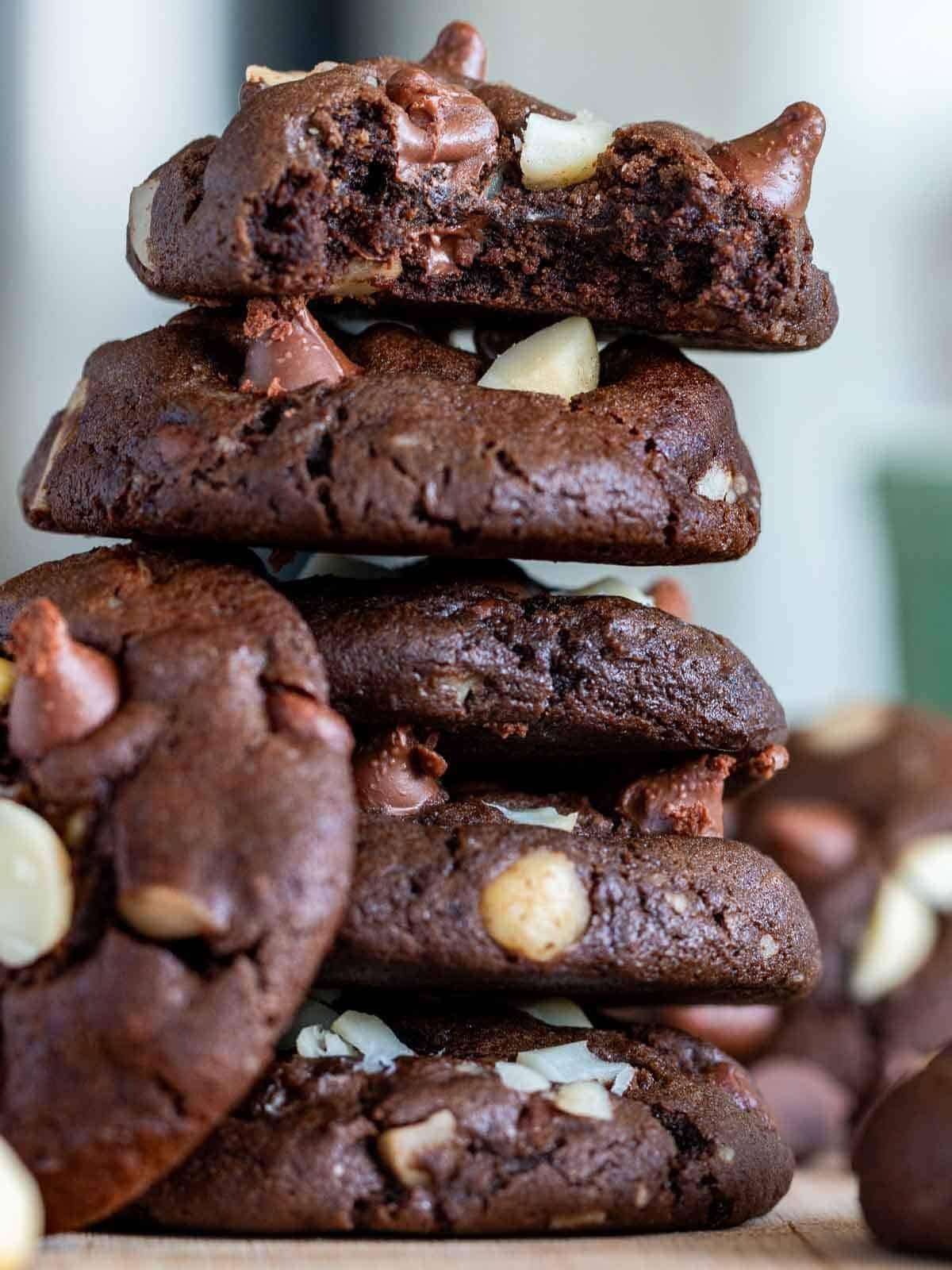 Dark chocolate macadamia nut cookies stacked up with a bite out of one on the top. 