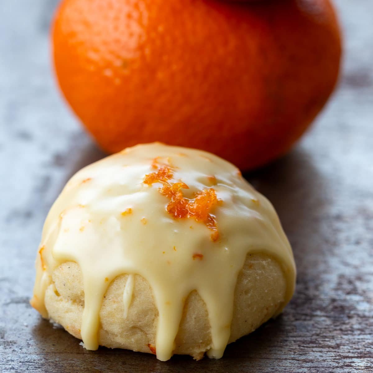 Italian orange cookie with the icing dripping down the sides of the cookie with a mandarin orange. 