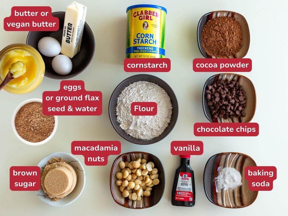 Wet and dry ingredients to make fudgy chocolate cookies with macadamia nuts laid out on a beige board along with some substitution ideas. 